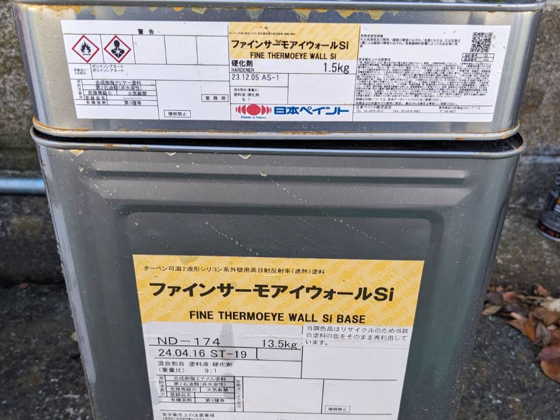 11_0 | 外壁塗装は神奈川県横浜市の塗装職人 Two metal cans stacked outdoors with yellow/white product labels in Japanese, showing