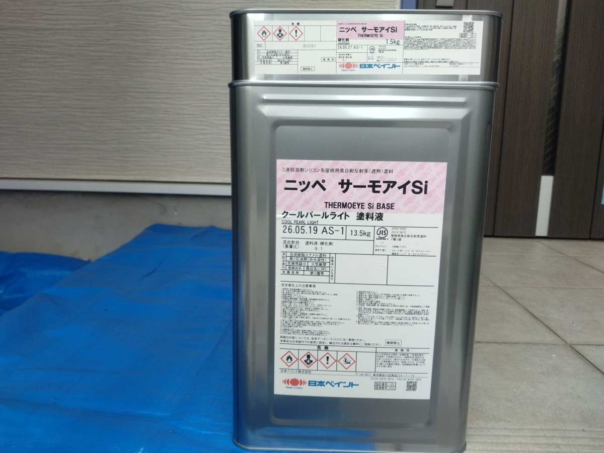 DCP PHOTO | 外壁塗装は神奈川県横浜市の塗装職人 Metal industrial canister with Japanese labeling, likely a paint or coating product, standing on a blue tarp beside a building exterior.