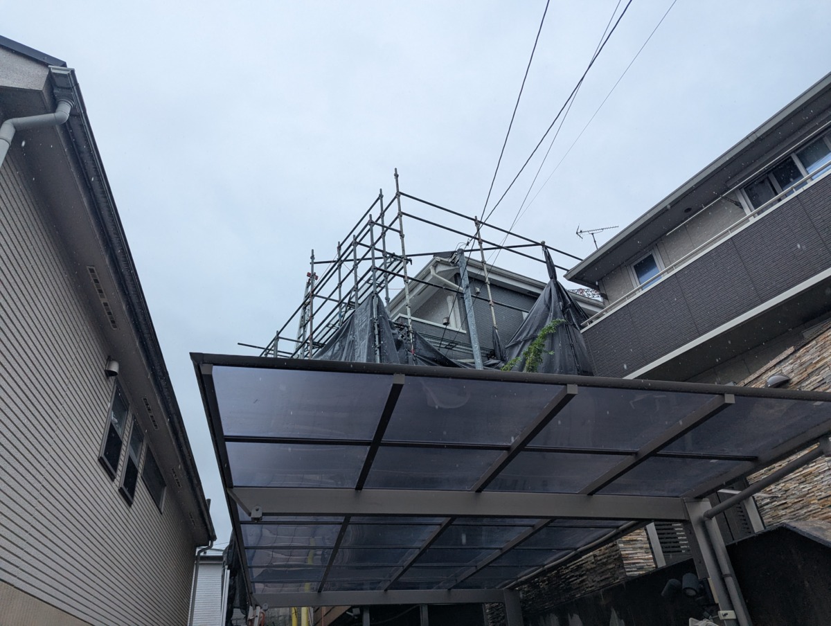 Rooftop construction scaffolding with tarps between two houses; power lines run overhead.