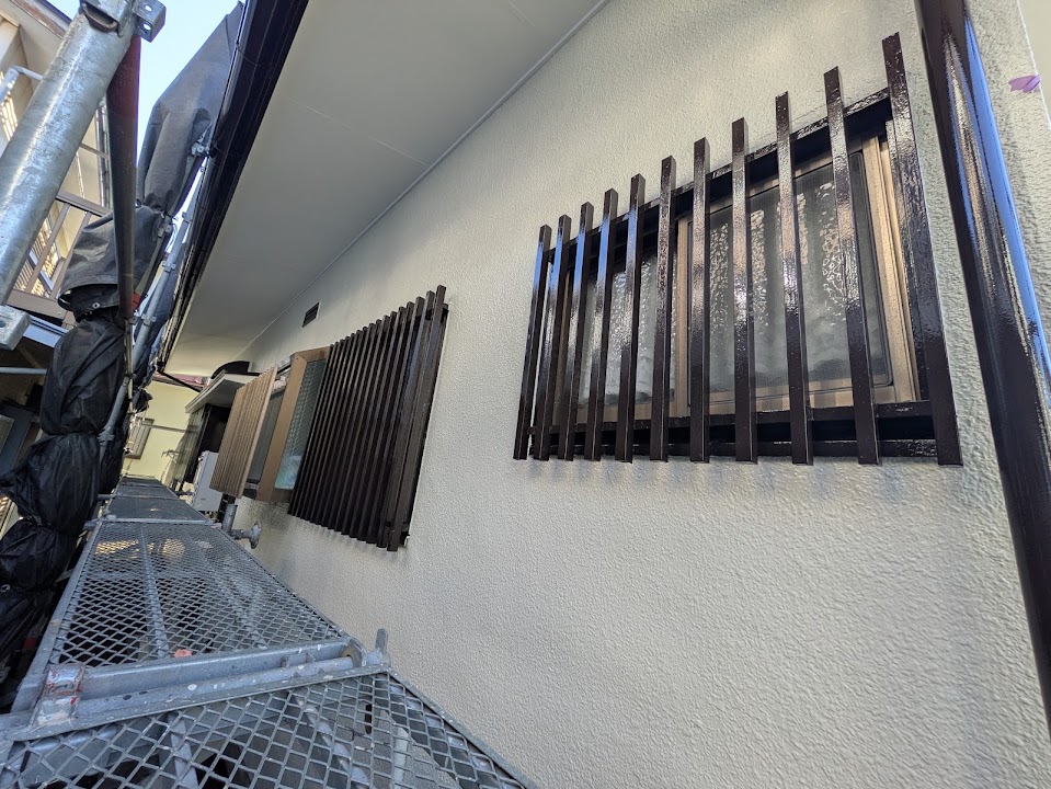 03-wall-finish | 外壁塗装は神奈川県横浜市の塗装職人 Exterior wall of a building under renovation; windows have black metal bars and a metal scaffold platform runs along the wall.