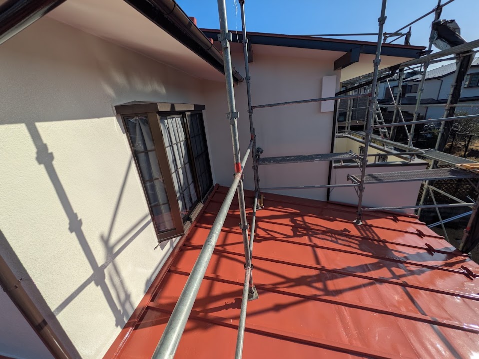 04-roof-finish | 外壁塗装は神奈川県横浜市の塗装職人 Scaffolding erected around the exterior of a beige house with a red metal roof on a sunny day.
