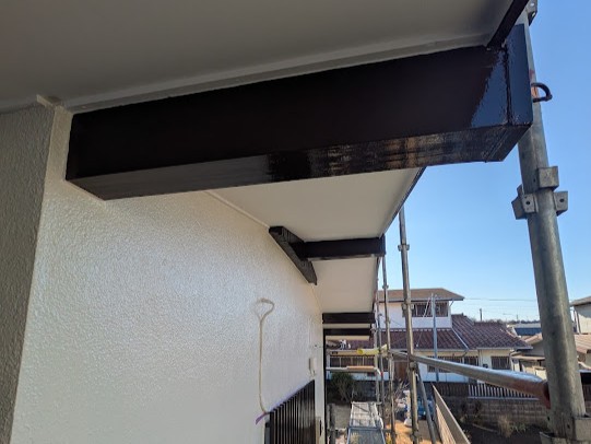 05-eaves-finish | 外壁塗装は神奈川県横浜市の塗装職人 Black steel beams attached under the building’s eaves, with scaffolding along the white exterior wall.
