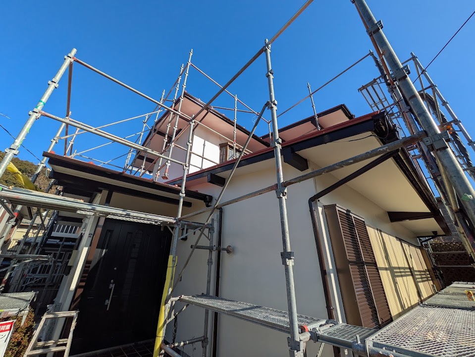 06-exterior-finish | 外壁塗装は神奈川県横浜市の塗装職人 Two-story house under construction encircled by metal scaffolding and ladders against a clear blue sky.