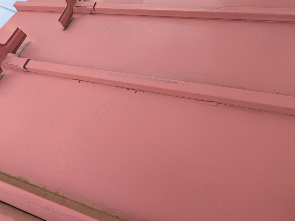 08-roof-before | 外壁塗装は神奈川県横浜市の塗装職人 Close-up of pink metal roof panels with a long horizontal seam showing slight cracking and wear along the flashing.