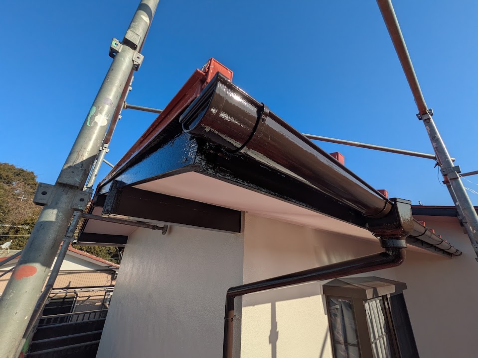 Scaffolding around a white house with a glossy black gutter and downspout under construction against a clear blue sky.