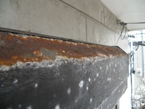 koushin_CIMG1276-1 | 外壁塗装は神奈川県横浜市の塗装職人 Rusty, corroded steel beam along a concrete ledge under an overhang, showing surface oxidation and weathering.