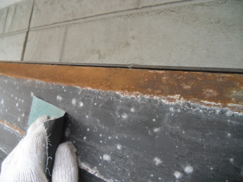 koushin_CIMG1280-1 | 外壁塗装は神奈川県横浜市の塗装職人 Worker wearing white gloves scrapes a rusty metal edge along a concrete wall area.