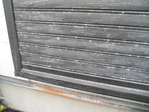 koushin_CIMG1287-1 | 外壁塗装は神奈川県横浜市の塗装職人 Closed dark metal rolling shutter with dust and rust along the bottom edge.