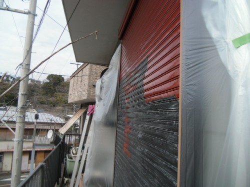 koushin_CIMG1292-1 | 外壁塗装は神奈川県横浜市の塗装職人 Storefront with a red metal shutter covered in plastic wrap during renovation, with a ladder and construction debris nearby.