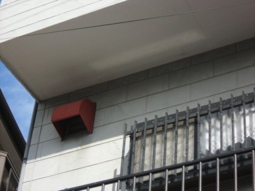 koushin_CIMG1295-1 | 外壁塗装は神奈川県横浜市の塗装職人 Red metal vent/box attached to a light-gray brick wall above a barred window under an overhang.