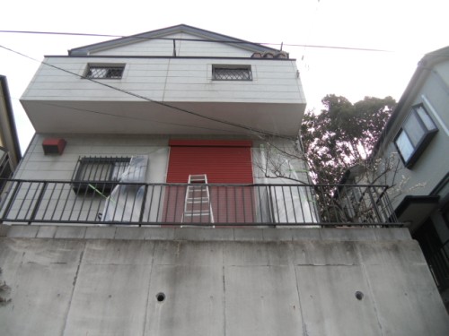 koushin_CIMG1298-1 | 外壁塗装は神奈川県横浜市の塗装職人 Facade of a multi-story building with a closed red shutter on the balcony, a ladder leaning against the railing, and a concrete front wall.