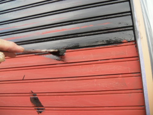 koushin_CIMG1300-1 | 外壁塗装は神奈川県横浜市の塗装職人 Close-up of a hand painting a red metal rolling shutter with black paint.