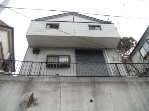 koushin_CIMG1304-1 | 外壁塗装は神奈川県横浜市の塗装職人 Two-story gray house seen from a low angle, with a balcony and metal railing along a concrete retaining wall.