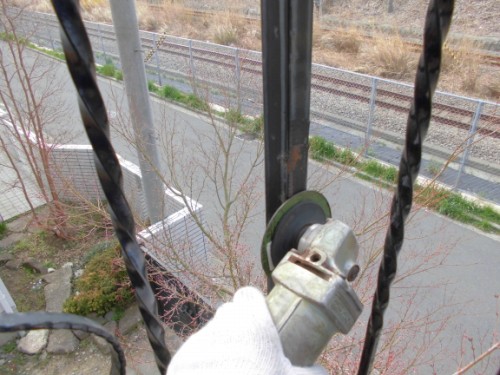 Gloved hand operating a grinder with a cut-off wheel against a metal railing near railway tracks.