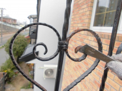Gloved hand bending a decorative heart-shaped wrought-iron railing on a brick house.
