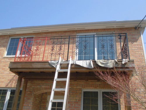 Ladder leaning against a brick house balcony on the second floor, with a metal railing and tarps covering the deck area