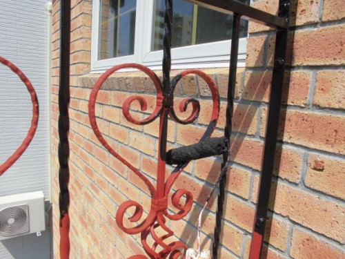 Decorative red wrought-iron railing with heart shapes against a brick wall near a window.