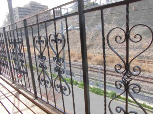 Decorative iron balcony railing with heart-shaped ornaments; train tracks visible beyond. (informative)