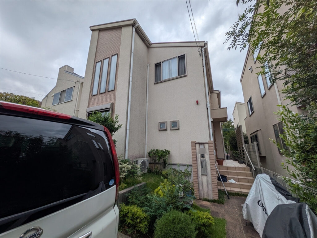 Front view of a two-story beige house with tall narrow windows, a small garden, and a white van in the foreground.