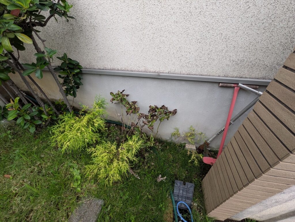植栽の後ろに続く施工前の基礎と外壁