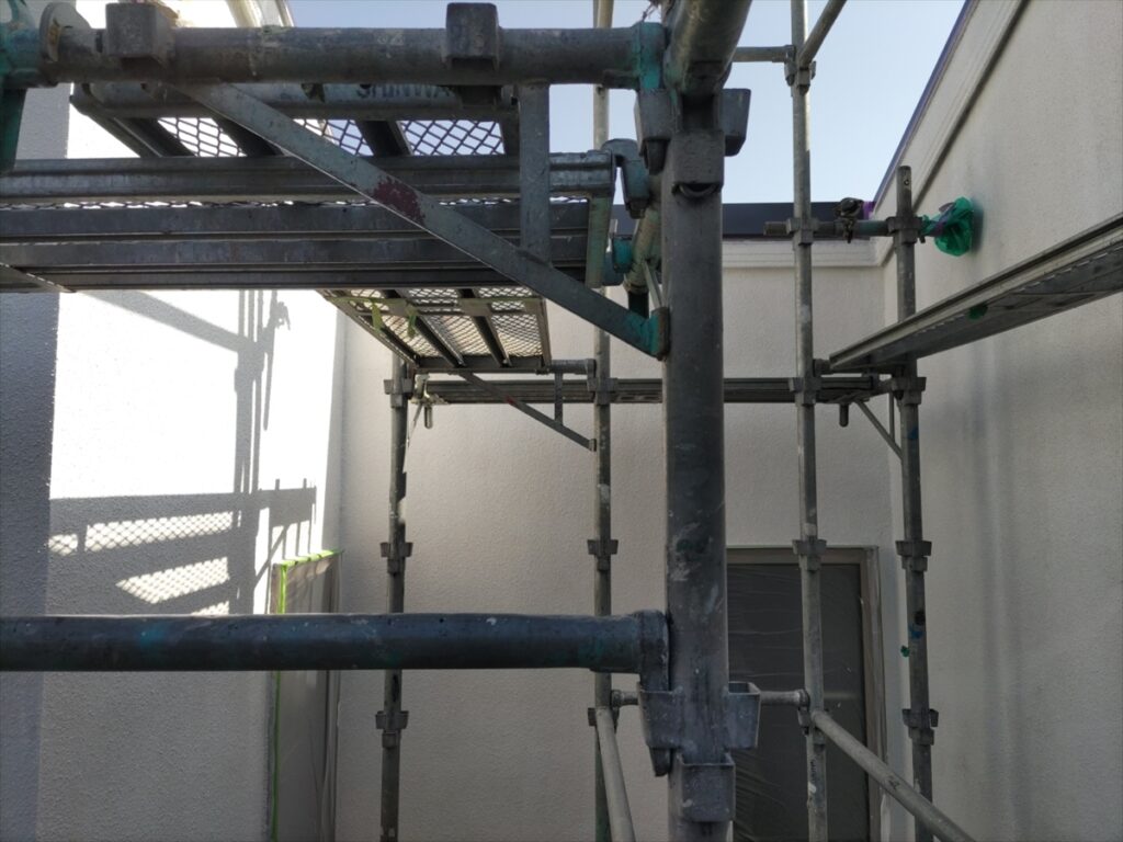 足場越しに見上げた白い外壁と配管