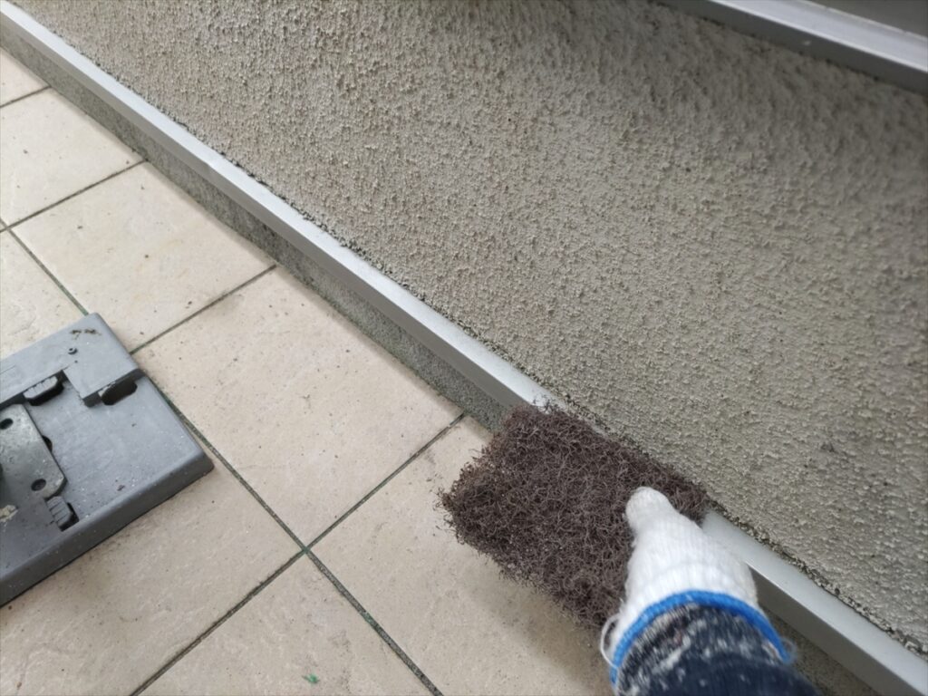 外壁下端の水切りに研磨材を当てる手元