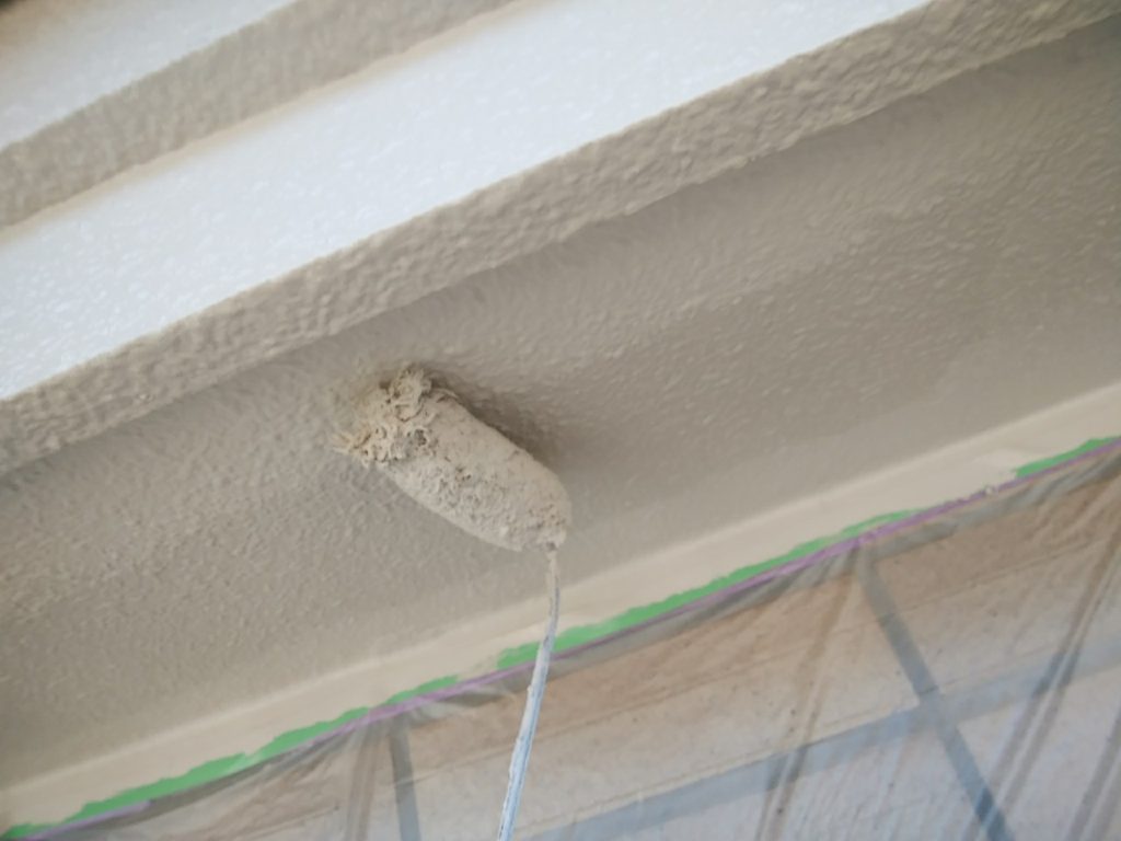 Close-up of a textured coating being rolled onto a ceiling, with plastic drop cloth and a taped edge visible.