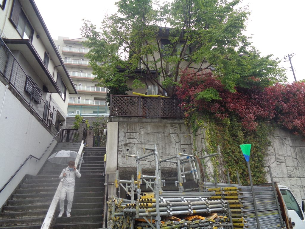 Person in white with a transparent umbrella walks down a concrete staircase beside a construction area with metal scaffolding and pipes on the ground.