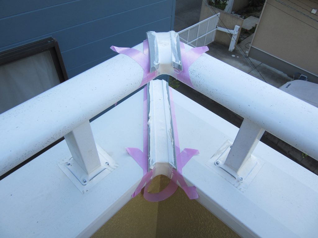 Close-up of roof peak showing white metal rails, pink painter’s tape, and foam-filled joint being prepared for repair at the valley edge of a building roof.