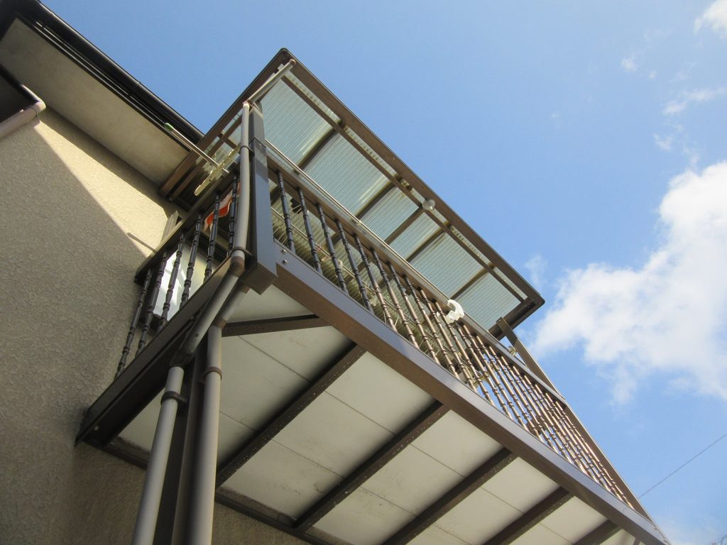 Low-angle view of a balcony with brown metal railing and a glass canopy against a blue sky