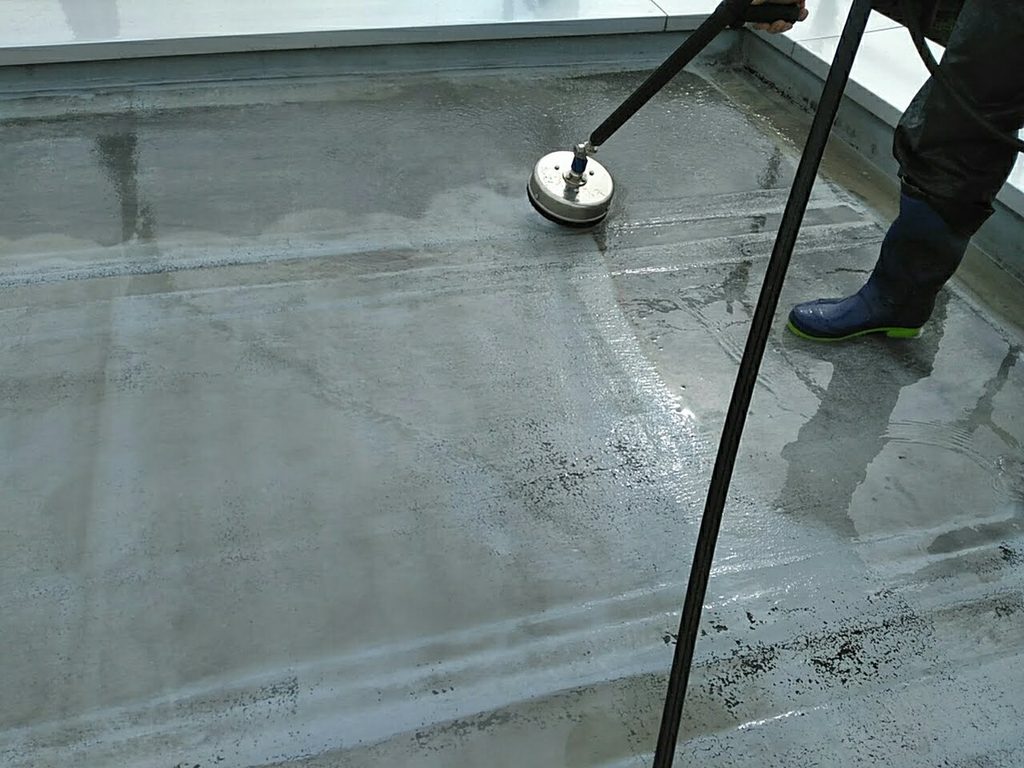 Worker in blue boots operates a floor grinder on a wet concrete surface.