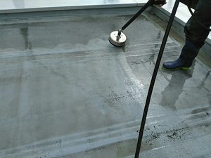 Worker in blue boots operates a floor grinder on a wet concrete surface.