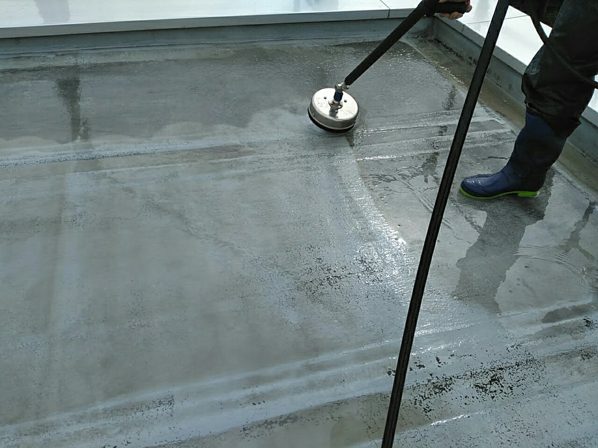 Worker in blue boots operates a floor grinder on a wet concrete surface.