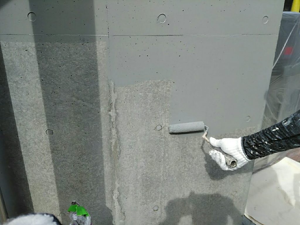 Person wearing gloves with a paint roller applying gray concrete paint to a wall surface