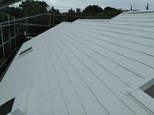 White pitched roof with metal panels under construction, surrounded by scaffolding and a cloudy sky.