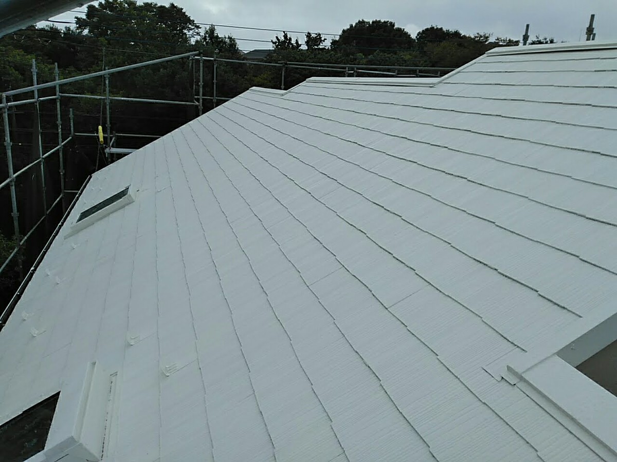 White pitched roof with metal panels under construction, surrounded by scaffolding and a cloudy sky.